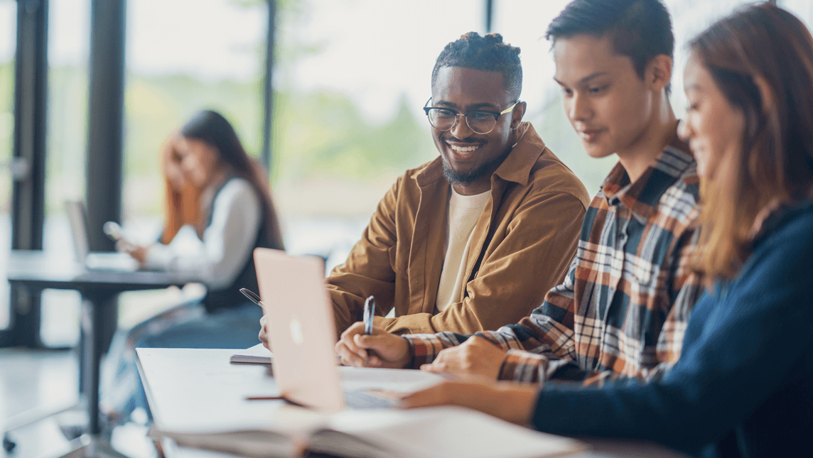Three University students are seen sitting together in class as they work together on an assignment.