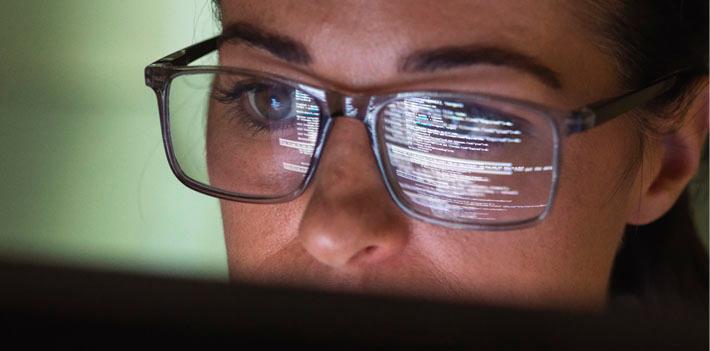 A programmer looks at a computer screen with code projects on her glasses.