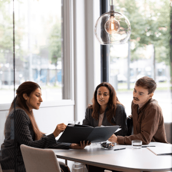 Female real estate agent showing floor plan to young customers while sitting at desk in office