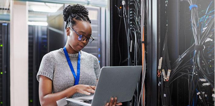 An IT worker looks at a laptop in a control room.