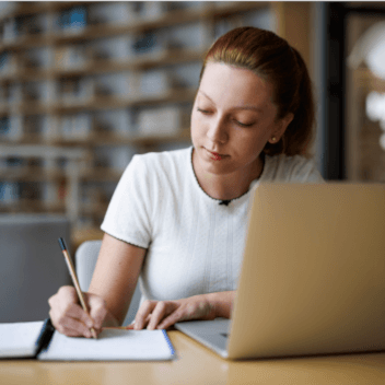 Female student taking notes while studying in library.