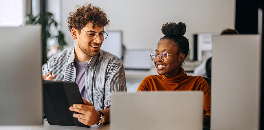 A male and female colleague working at laptops together.