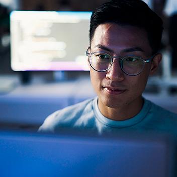 A man wearing glasses looking at a computer screen.