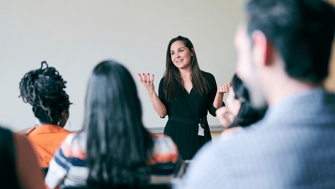 Happy teacher gesturing and explaining students in classroom
