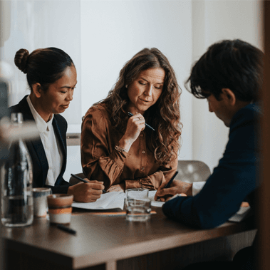 Business people writing while discussing strategy with colleagues sitting at desk in office.