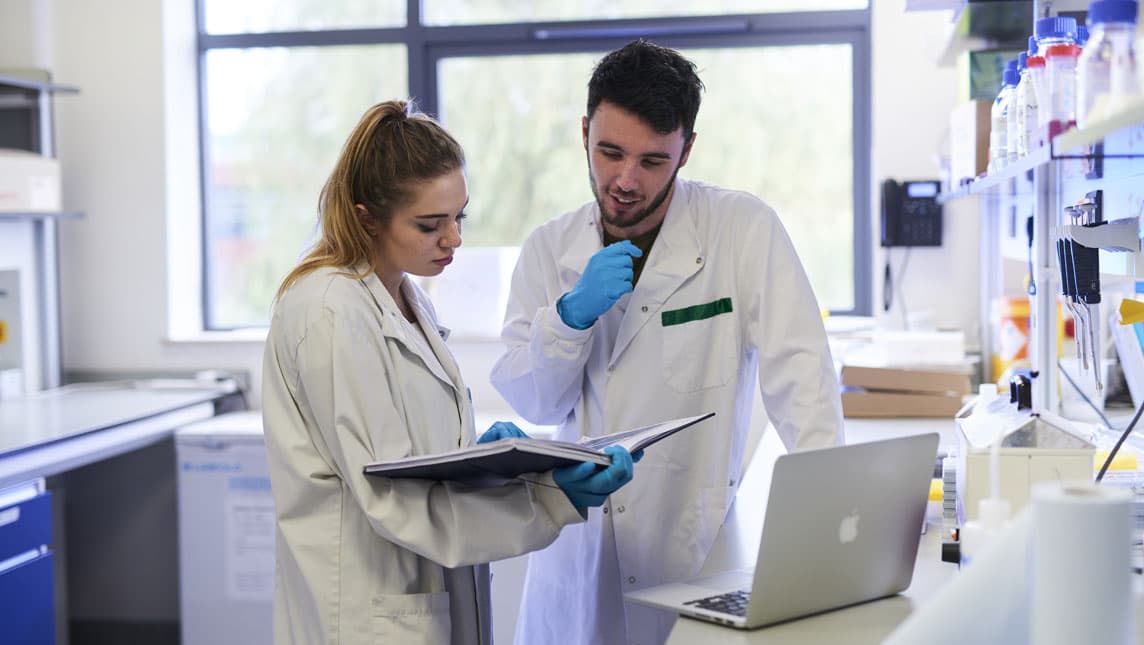 Two medical students work from a laptop and notebook in a hospital laboratory.