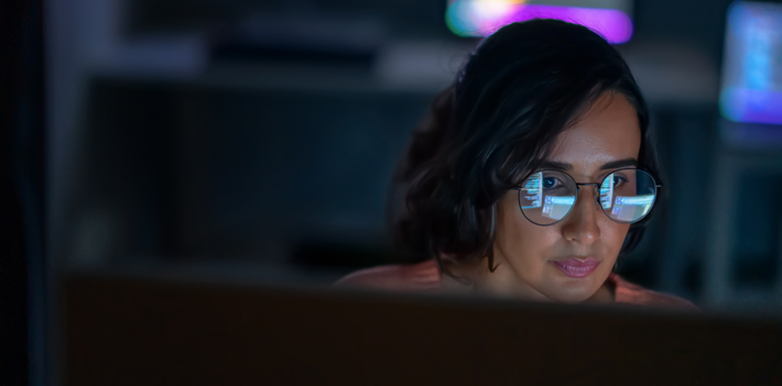 A computer operator stares at a screen of code that reflects on their glasses.