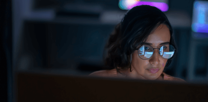 A computer operator stares at a screen of code that reflects on their glasses.