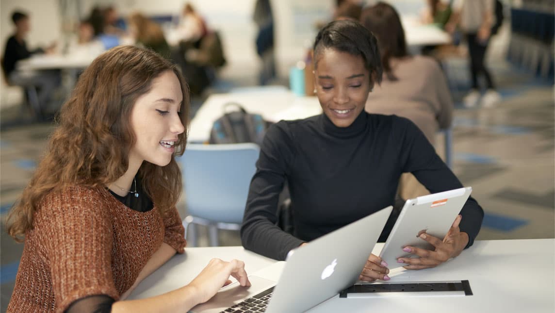 Two students happily in discussion with a tablet and a laptop.
