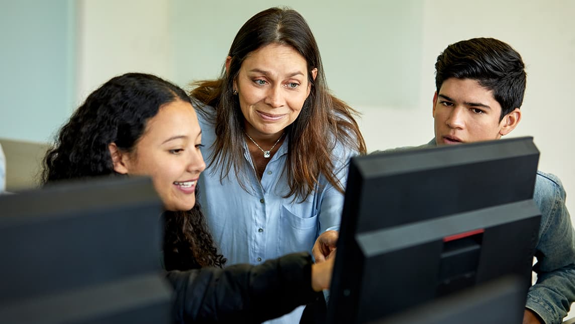 A teacher talks with students in front of a computer.