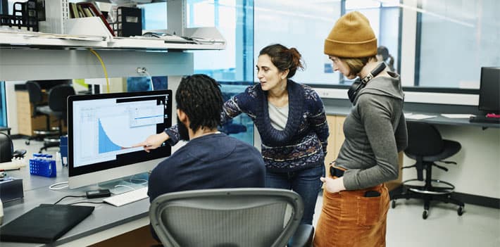 Three colleagues review data on a computer screen.