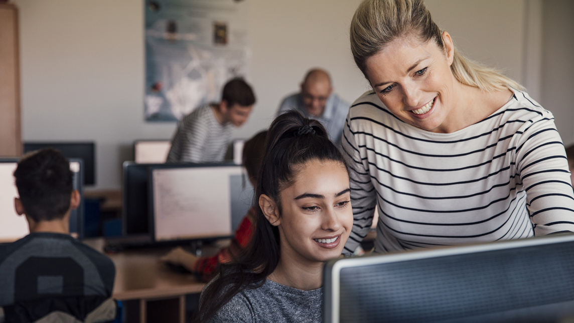 A female pupil is sitting behind a computer receiving help in lesson