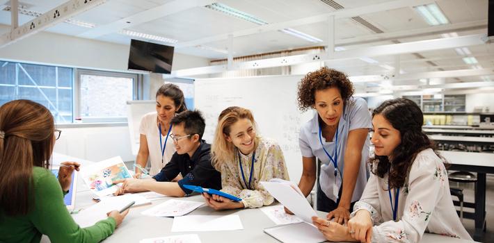 Female students and teachers discuss their work in a classroom.