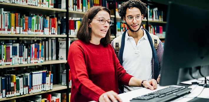 A librarian helps a student locate a book using a computer.