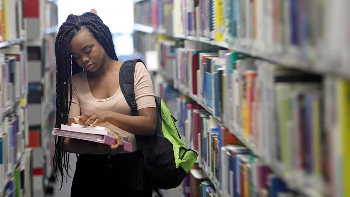 A student studying in a library carrying books and files.