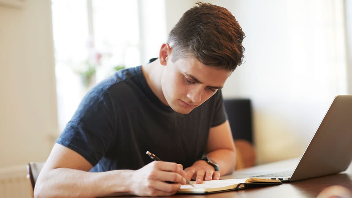 A student makes notes during an online exam.