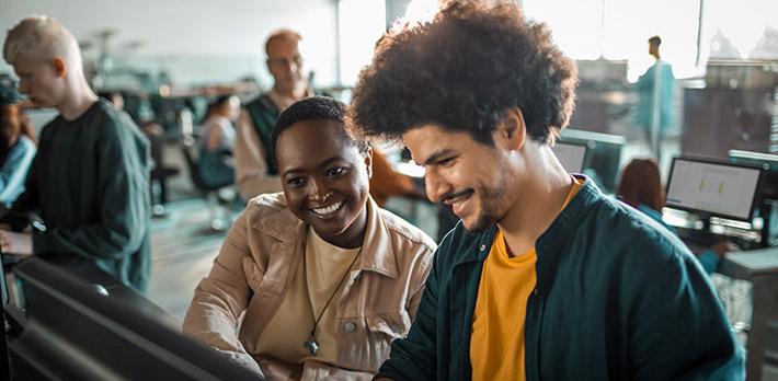 Students smile as they collaborate in a computer room on a university campus.