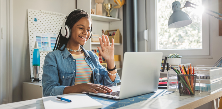 Teenage girl studding at home. She is sitting at the table and using laptop for homework.