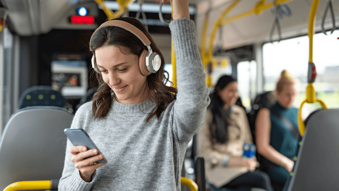 Happy woman using mobile phone and headphones while listening a music in a bus