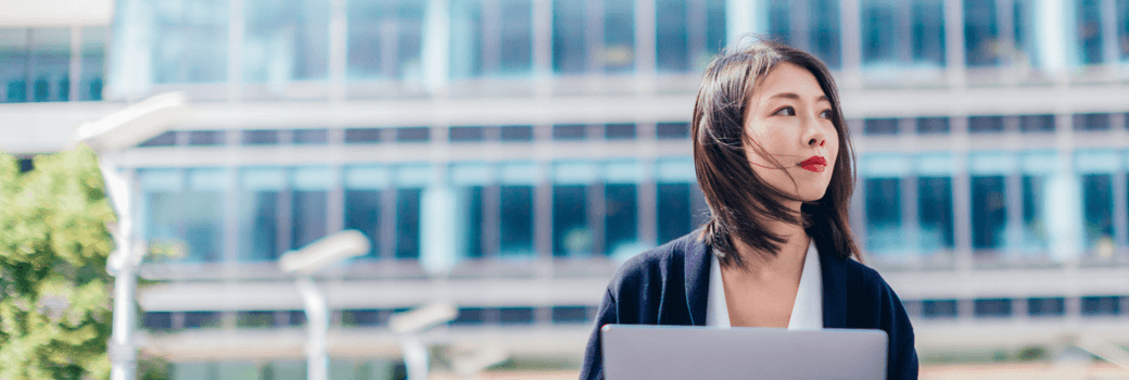 A woman uses her laptop outside a building.