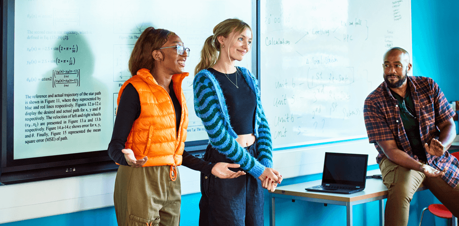 Technical college students standing at front of class presenting project with teacher looking on