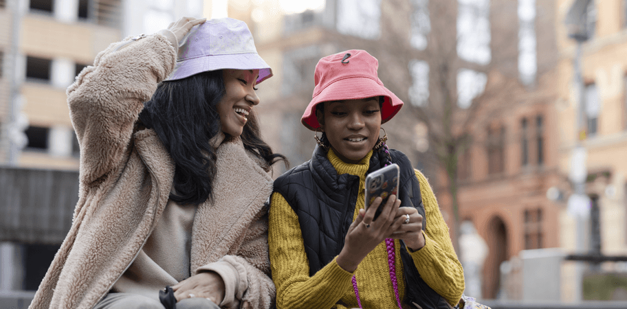 Two young women in urban setting, looking at phone.