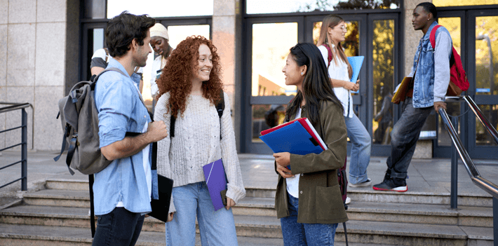 Students smile and talk outside a college