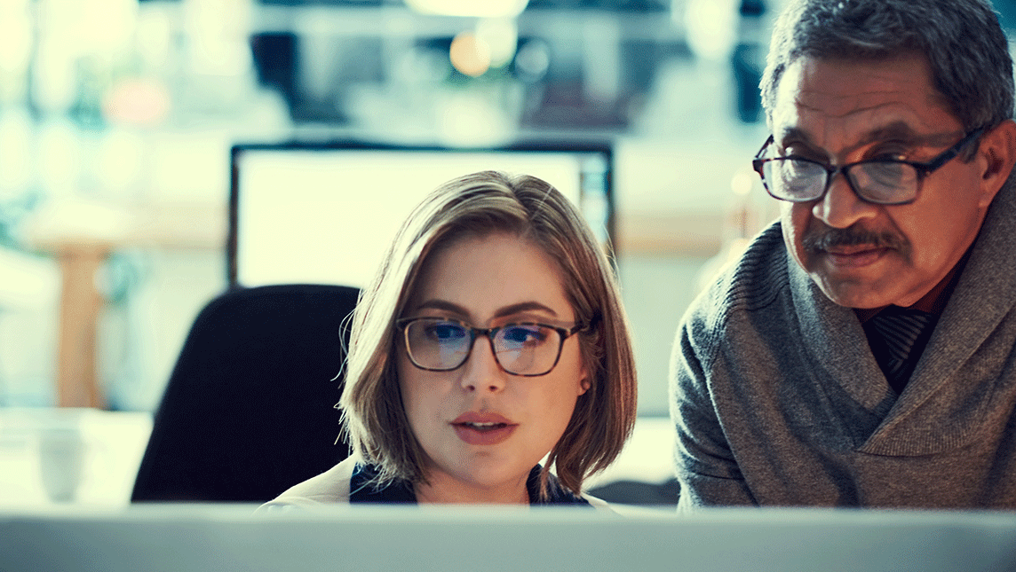 Two colleagues look at a computer screen in an office.